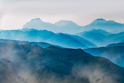 High mountains with green slopes in dense fog. Layers of mountains in the haze during sunset. Multilayered misty mountains. Krasnaya Polyana, Sochi, Russia.