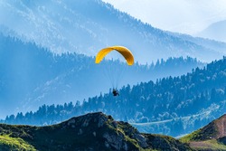 Yellow paraglider over the Green Mountain slope. Paraglider fly over mountain slope on sunny summer day,
