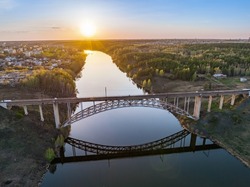 Beautiful view of the arched railway bridge across the Iset River in the city of Kamenkk-Uralsky at sunset in spring. Kamensk-Uralskiy, Sverdlovsk region, Ural mountains, Russia. Aerial view