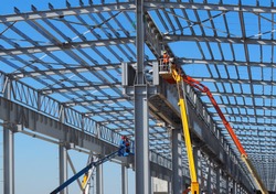 Workers on aerial work platforms build the metal structure of the roof of a large building.