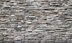 Stone cladding wall made of striped stacked bricks of natural brown and gray rocks .