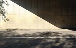 Grunge concrete wall of an underpass divided in two by the shadow of the bridge. Sidewalk and two lane road in front. Background for copy space.