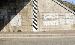Stone block wall at the entry of a road tunnel with erased graffiti and black and white stripes of the street border. Sidewalk and asphalt road in front. Background for copy space.