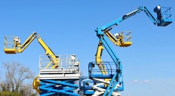 Group of work aerial platforms,  cherry pickers and scissor lifts models, against blue sky.