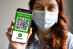 Covid-19 Health Passport. Traveler woman wearing a face mask holding a passport, ticket pass and smartphone with digital health passport app.