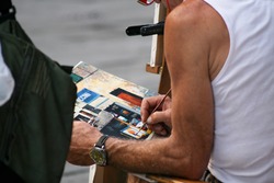 Summer. Italy. Florence. The street artist paints a picture with oil paints and a thin brush.