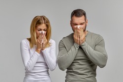 A man and a woman blow their nose in a napkin on an isolated white background. Portrait of people with cloth in their hands. The concept of treating allergies or colds.