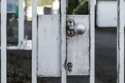 vintage old metal gate with stainless and rusty handle knob and lock is part of aged fence around home to keep out unauthorized from entrance and secure the privacy by this locked door