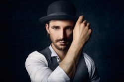 old vintage styled portrait of serious englishman with hand at hat look neutral at camera with cold unfeeling eyes could be a criminal stylish and modern man with nostalgic fashion lifestyle