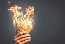 Burning Euro banknotes held by a hand