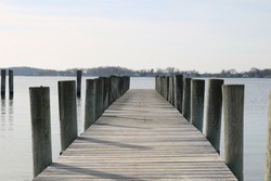 Long weathered wooden dock pier in coastal seaside harbor beach in winter