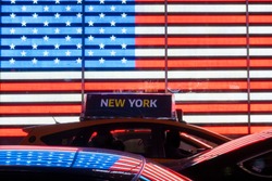 Some cars and a taxi are lined up in Times Square under an illuminated American flag. Manhattan, New York city, USA.
