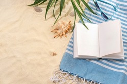 Top view of striped blue towel with book and sunglasses on sandy beach. Background with copy space and visible sand texture.