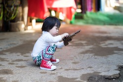 Asian baby girl sitting and playing wood gun.She ware white long shirt tile long leg and red shoes.