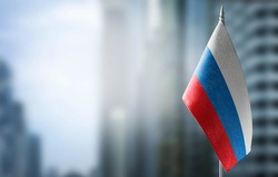 A small flag of Russia on the background of an urban abstract blurred background.