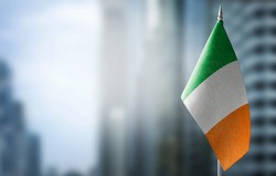 A small flag of Ireland on the background of an urban abstract blurred background.