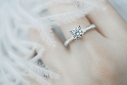 Close up of elegant diamond ring on the finger with feather and gray Scarf background. Diamond ring.