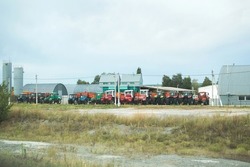 Many tractors in agricultural enterprise, motor transport depot, on cloudy day in country