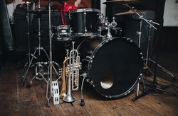 A black drum kit and a microphone stand are on stage and next to them are two trumpets (alto and bass) and a white tambourine. The concept of a live concert of a jazz band.