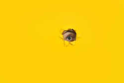 Right eye looking through a hole in a yellow paper. Voyeurism. Woman is watching the husband. A curious look. Jealousy, spying on or overhearing the concept. Copy space.