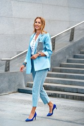 Women's modern business clothes in blue tones. Jeans in business style. Blue business jacket with brooch, cropped jeans, silver clutch and blue high heels. A woman in a white blouse with jewelry.