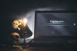 Illegal data copying concept. Cybercrime. Computer piracy background. Pirate hat, human skull, laptop and compact disc on a table.