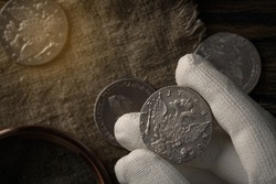Numismatics. Old collectible coins of silver on the table.  A collector in special gloves holds an old coin. Top view.