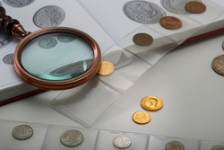 Numismatics. Old collectible coins and a magnifying glass on the table. Light background.