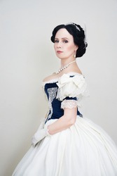 A beautiful elegant dark haired woman in a historic 1867 coronation dress on a white background looks at the camera