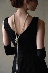 Beautiful woman figure in profile in a black dress and pearls in the style of 20-30 years of the XX century    