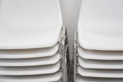 Close-up of white plastic chairs in a row waiting for visitors. White plastic chairs stand on top of each other against a white wall. High quality photo