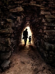 Silhouette of father and son in backlight in a small and dark stone tunnel: Image taken at Tulum in Mexico.