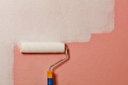 Close-up of a fleecy paint roller painting a pink wallpaper on a wall with white paint, copy space.
