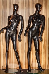 Two plastic mannequins in black color on glass round stands on a wooden striped background for demonstrating women's clothing.