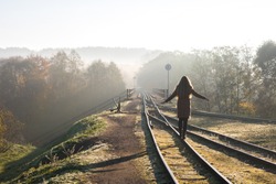 A girl is balancing on narrow gauge train tracks over bridge with sign no trespassing in Ankysciai, Lithuania