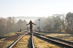 A girl is balancing on narrow gauge train tracks over bridge with sign no trespassing in Ankysciai, Lithuania