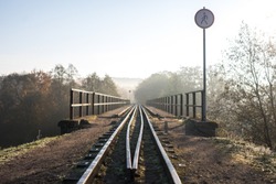 Narrow gauge train tracks passes over bridge with sign no trespassing and morning fog in Ankysciai, Lithuania