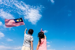 Unknown kids/brother and sister waving the Malaysia Flag. Independence Day & Merdeka Concept. Blue sky and copy space.