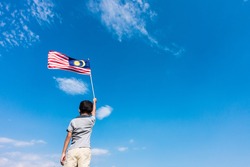 Unknown kid waving Malaysia Flag. Independence day and Merdeka Celebration. Blue sky and copy space.