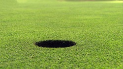 A hole on the golf course in close up view with green grass ground background.