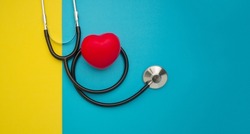 Top view of a stethoscope and a red heart shape on a yellow and blue background. Space for text. Medical and healthcare concept.