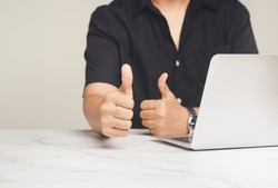 Positive concept. A businessman in a black short-sleeved shirt showing thumbs up to the success and best service while sitting at the table in the office. Customer service and satisfaction surveys
