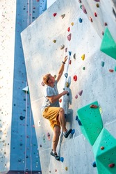 A male climber is rock climbing outdoors on an artificial boulder without a safety harness.