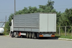Part of a big gray truck with a container on the asphalt road