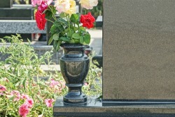 black marble vase with colored rose flowers at a gray granite monument on a grave in a cemetery