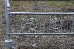 part of a gray old metal decorative fence made of iron bars overgrown with dry grass at the grave in the cemetery