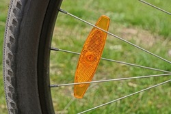 one red plastic reflector on the gray metal spokes of a black bicycle wheel against the background of green grass in nature