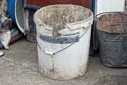 one large plastic broken white dirty bucket stands on gray asphalt on the streets near the wall