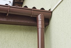 part of a brown plastic drainpipe on a gray concrete wall of a building on the street