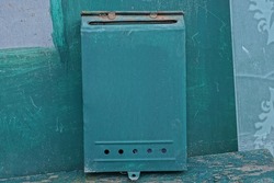 one green metal mailbox stands against the wall of the fence on the street